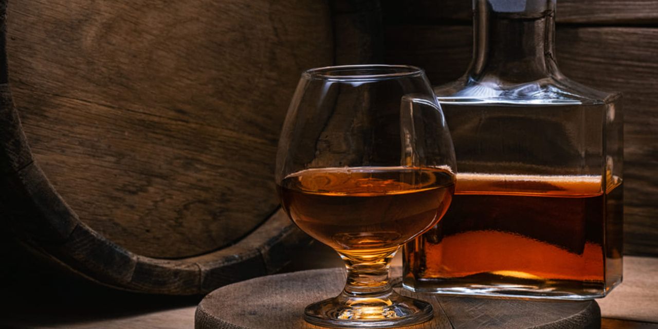 pahar si sticla de cognac in fata unui butoi de lemn folosit pentru maturarea coniacului pahar si sticla de cognac in fata unui butoi de lemn folosit pentru maturarea coniacului
