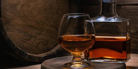 pahar si sticla de cognac in fata unui butoi de lemn folosit pentru maturarea coniacului pahar si sticla de cognac in fata unui butoi de lemn folosit pentru maturarea coniacului
